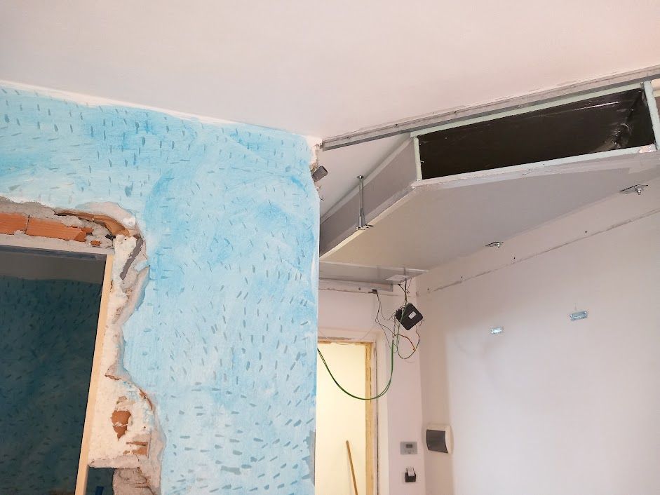 Stanza in costruzione con parete testurizzata blu e soffitto a vista con un rettangolo scuro.