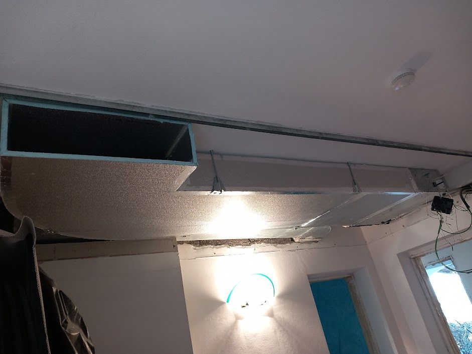 Condotti dell'aria su un soffitto bianco con una presa d'aria rettangolare, apparecchi di illuminazione e una porta.