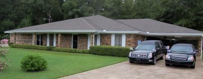 A brick house with a carport has two black cars parked under it.