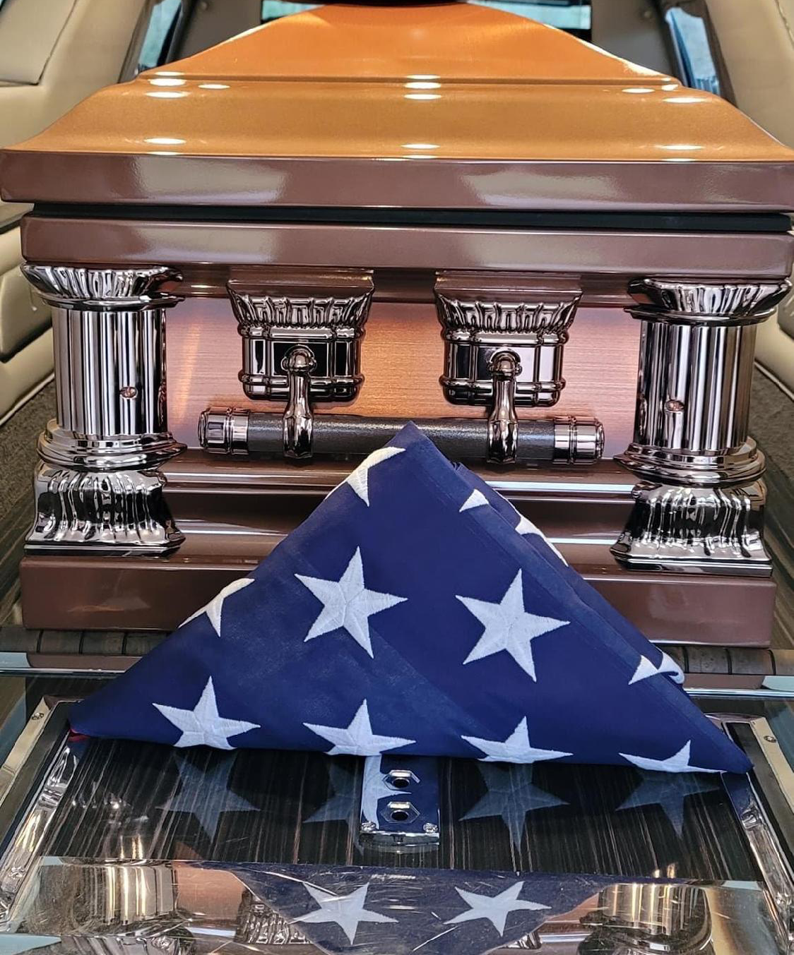 Coffin with an American flag folded on top, inside a hearse.