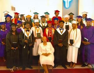 Group of graduates in caps and gowns pose for a photo in front of a church emblem.