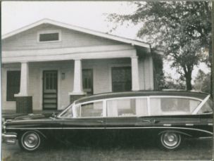 black and white image of house and black car in front of it