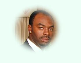 Man in a suit, headshot, looking at the viewer. Blurred white background, slight smile.