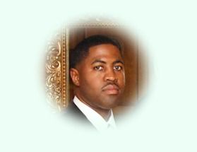 Man in a suit, looking toward the camera, in front of a decorative gold frame.