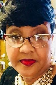 Woman wearing glasses, red lipstick, and pearl necklace, looking forward.