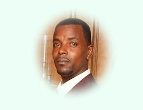 Man in a blazer and collared shirt, with a neutral expression, in a light-toned setting.