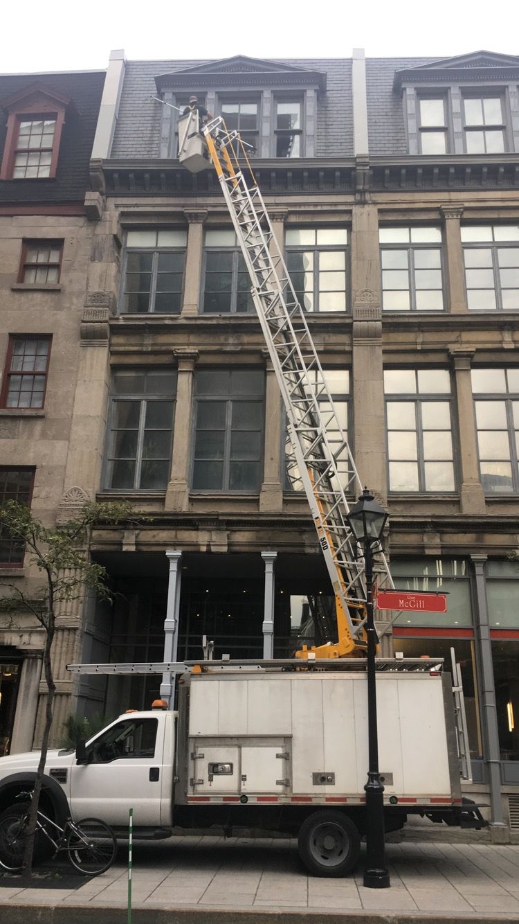 Un camion blanc avec une échelle attachée est garé devant un bâtiment.