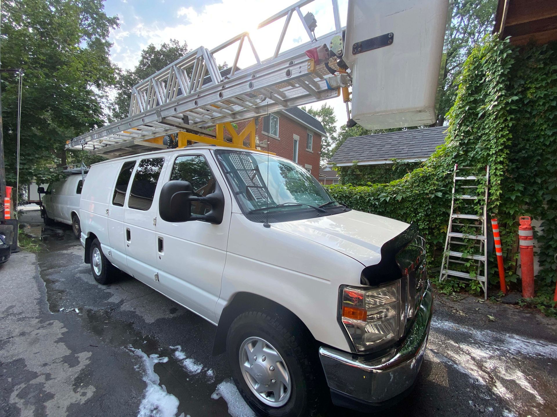 Une camionnette blanche avec une échelle dessus est garée sur le bord de la route.