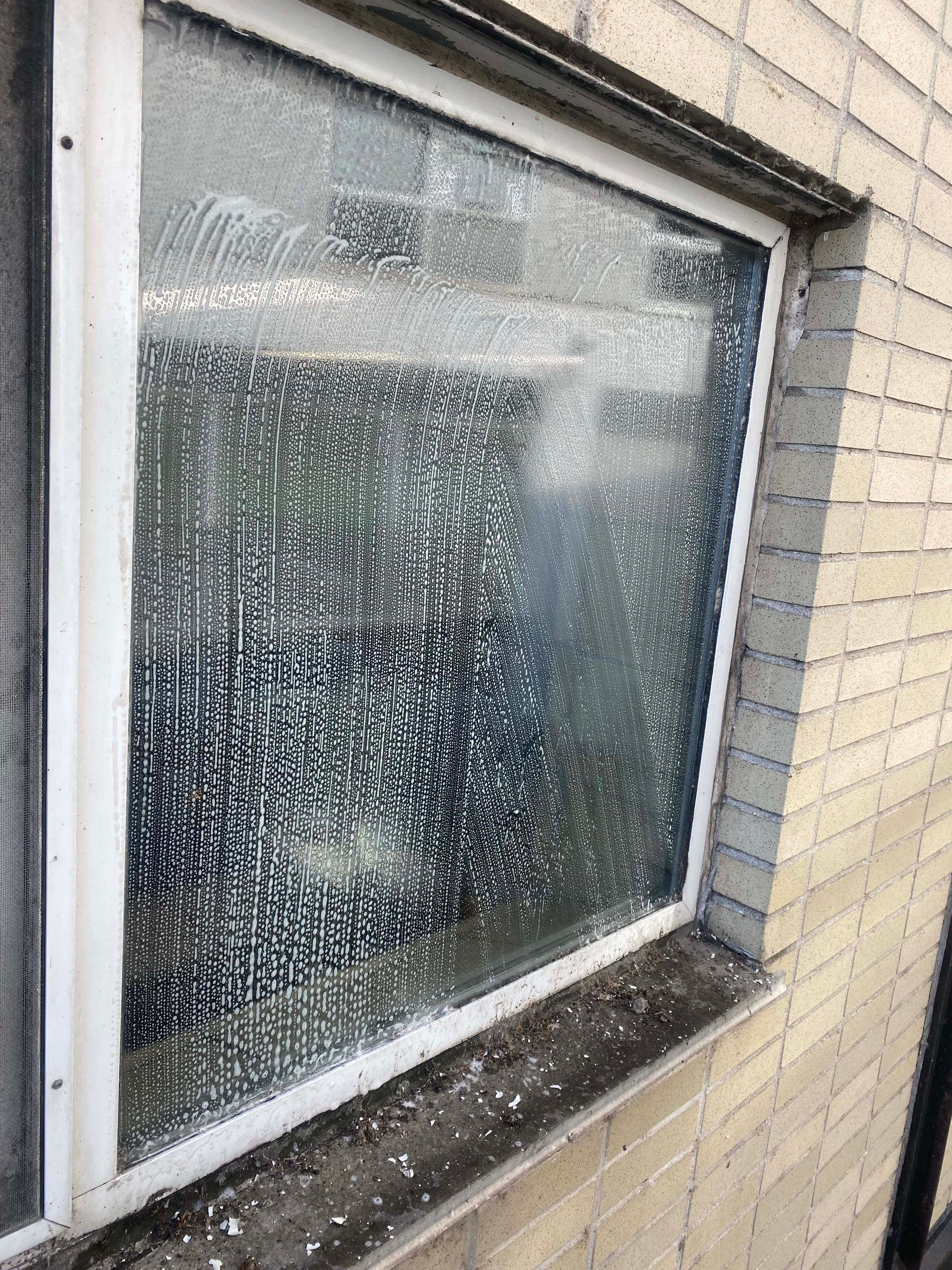 Une fenêtre sale avec un cadre blanc sur un mur de briques.