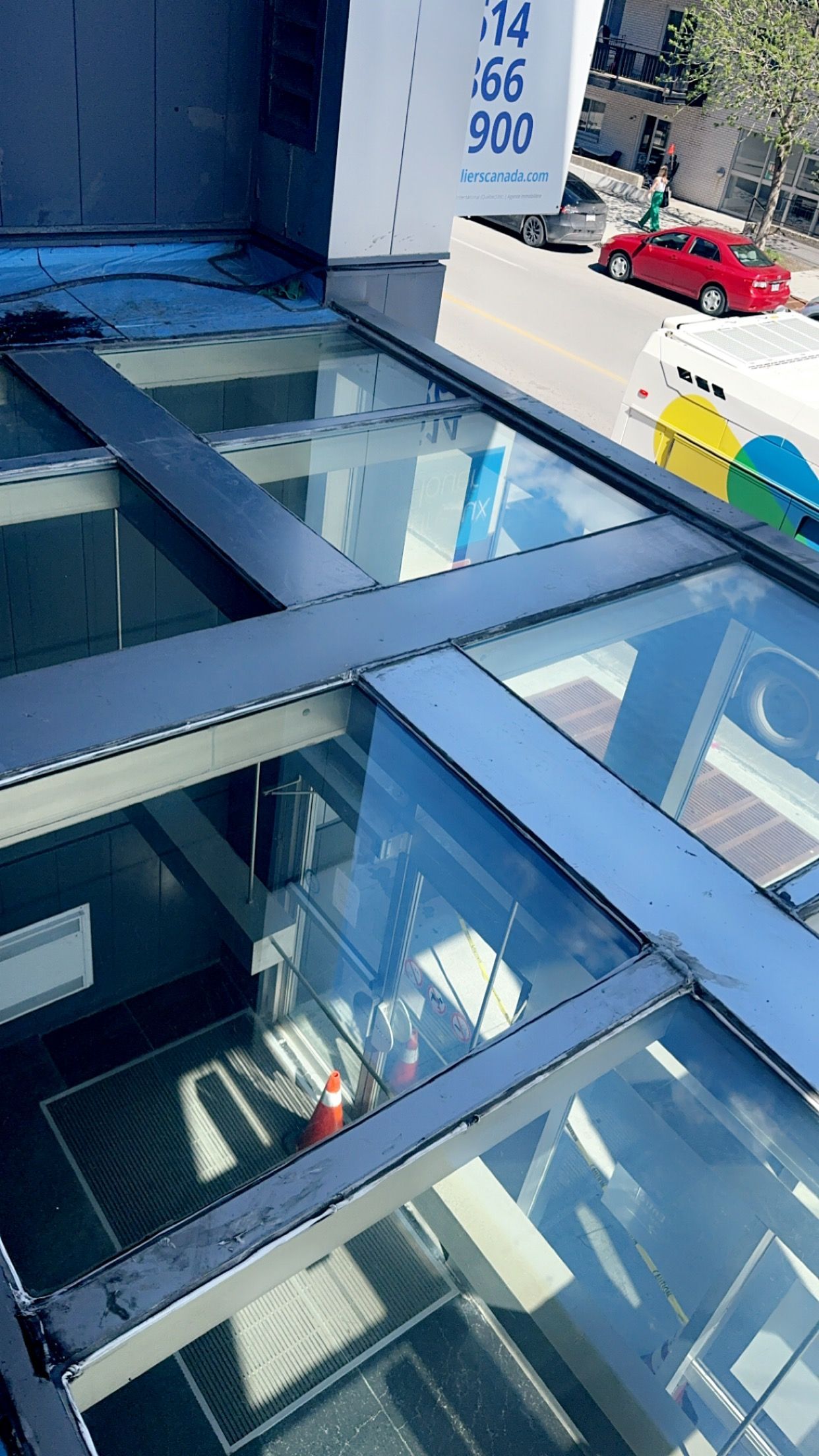 Un gros plan d'un toit en verre avec une voiture rouge en arrière-plan.