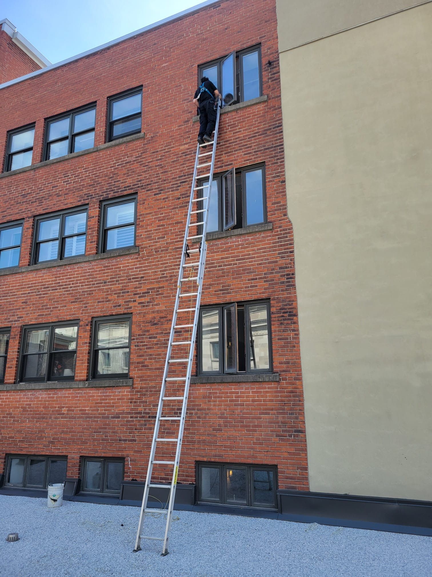 Un homme se tient debout sur une échelle sur le côté d'un bâtiment en briques et nettoie les fenêtres.