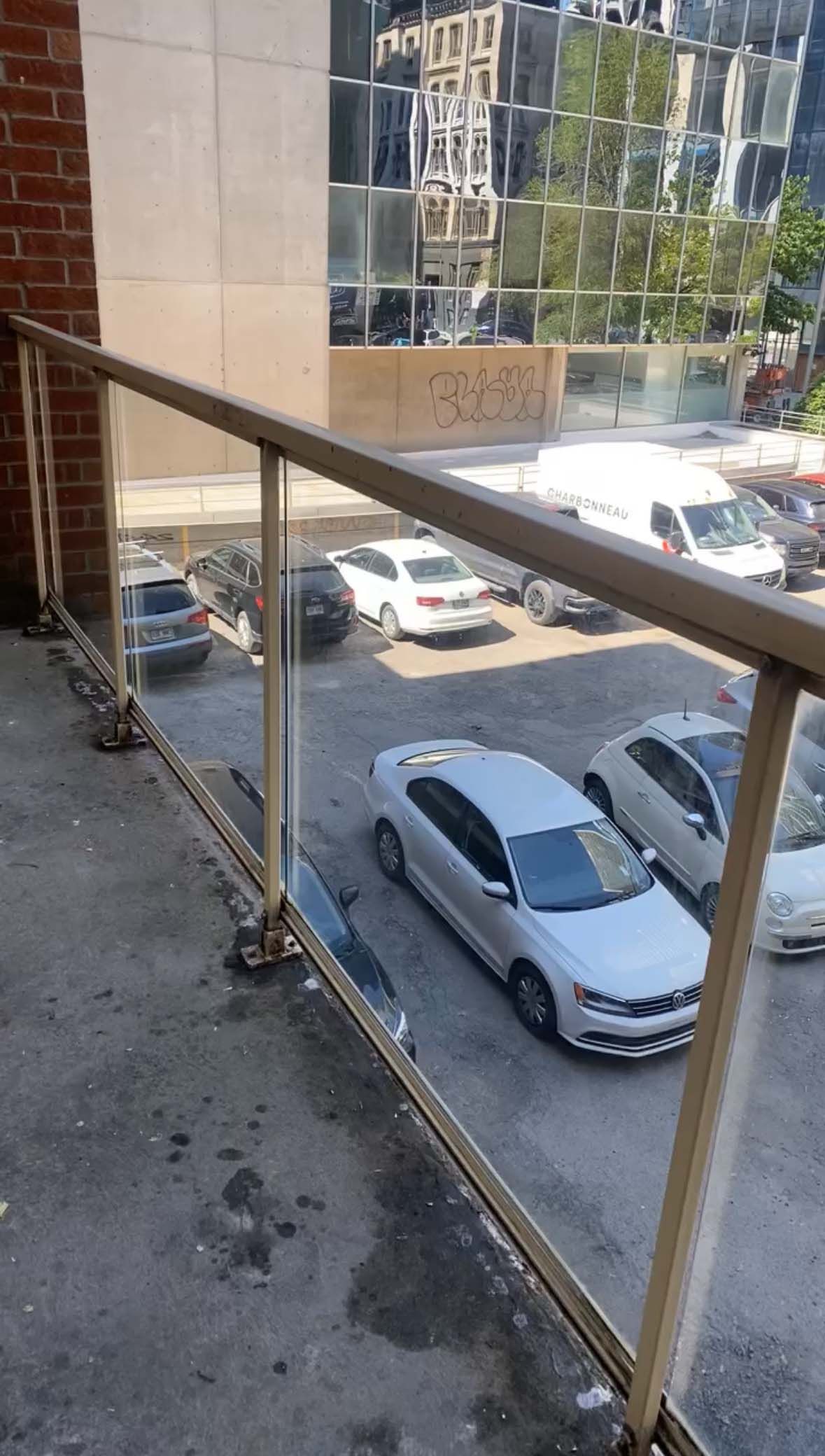 Un balcon avec vue sur un parking avec des voitures garées dedans.