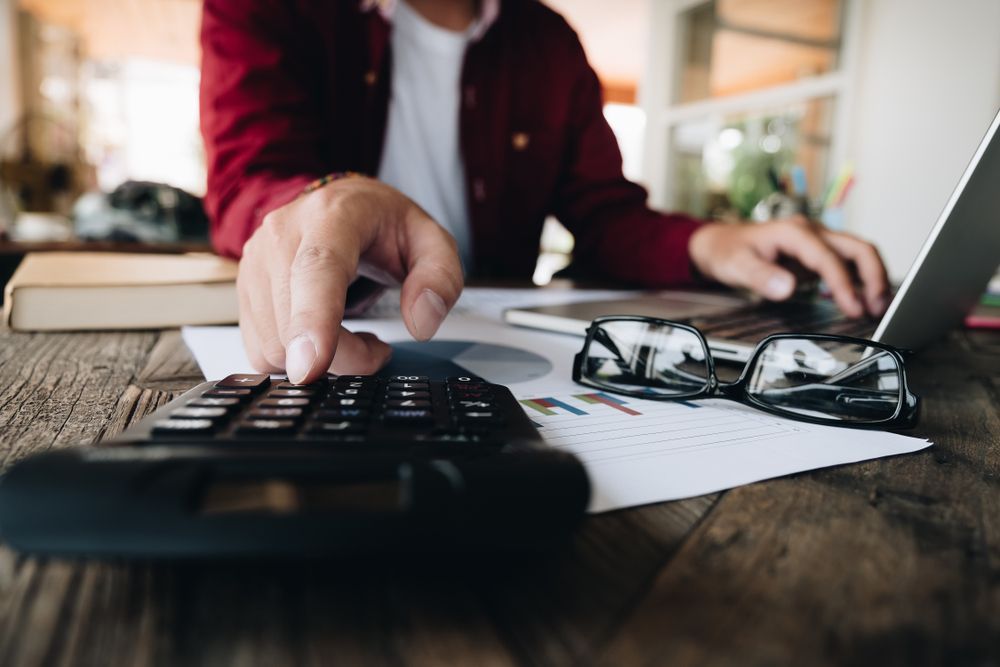A Man Is Using A Laptop And A Calculator At The Same Time — One Stop Bookkeeping in Ballina, NSW
