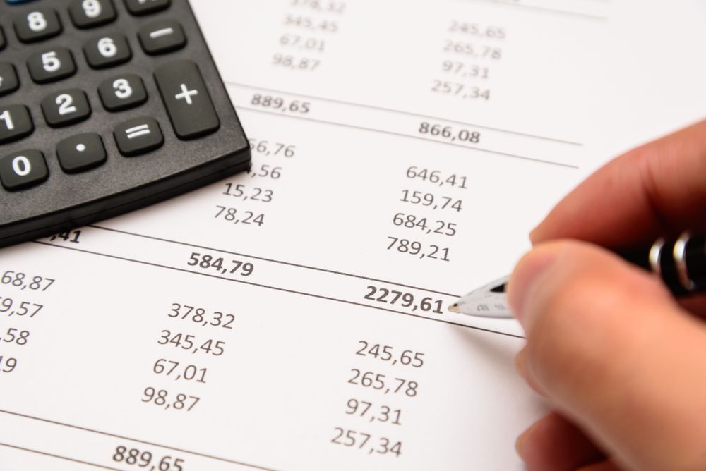 A Person Is Writing On A Piece Of Paper Next To A Calculator — One Stop Bookkeeping in Ballina, NSW