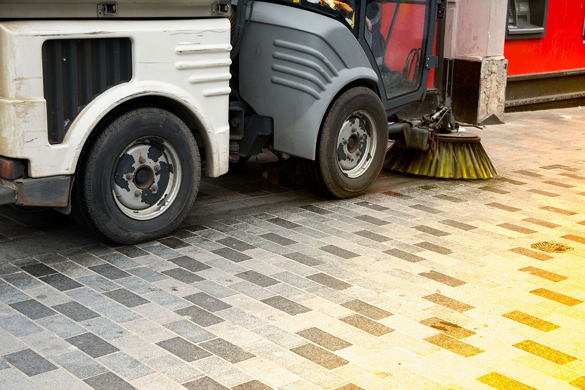 A street sweeper is cleaning the sidewalk with a broom.