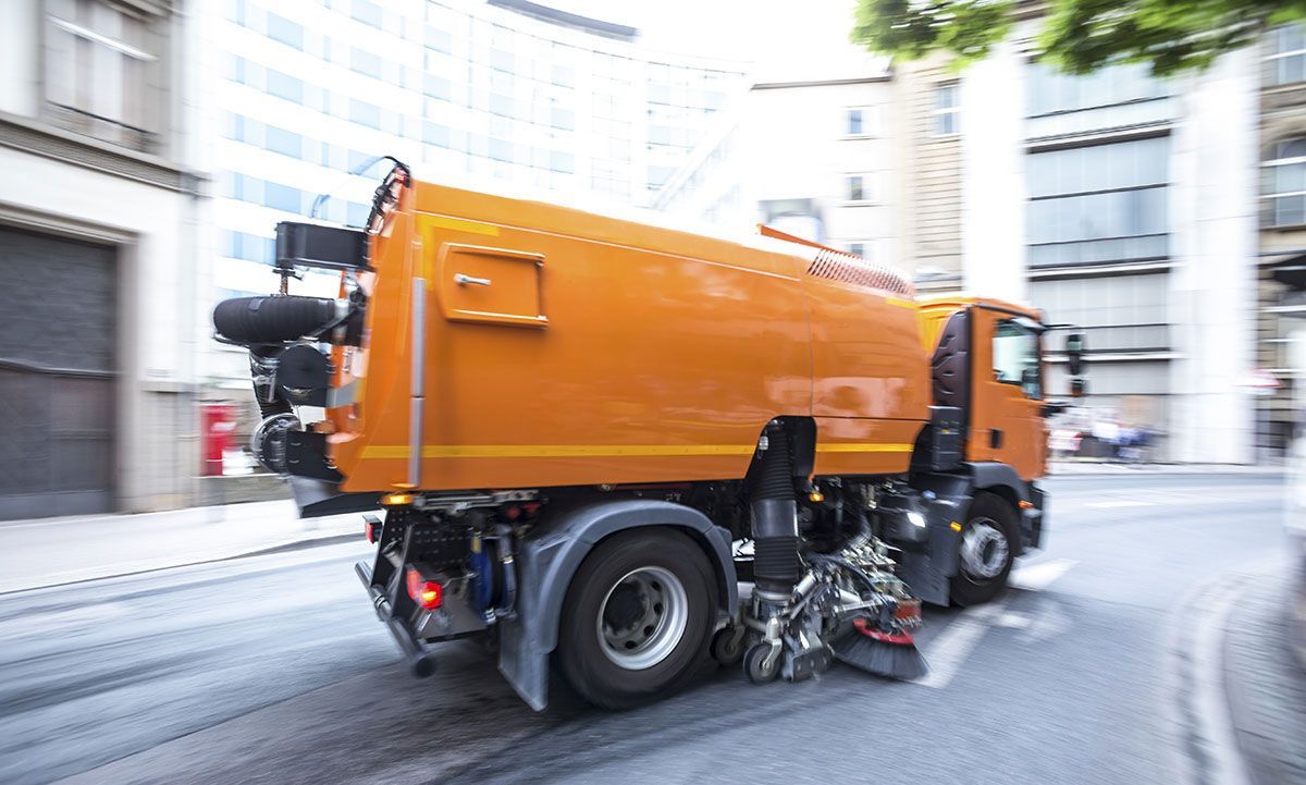 An orange street sweeper is driving down a city street.