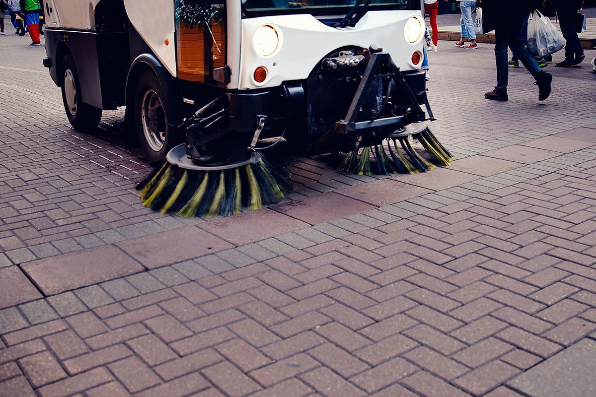 A street sweeper is driving down a brick sidewalk.