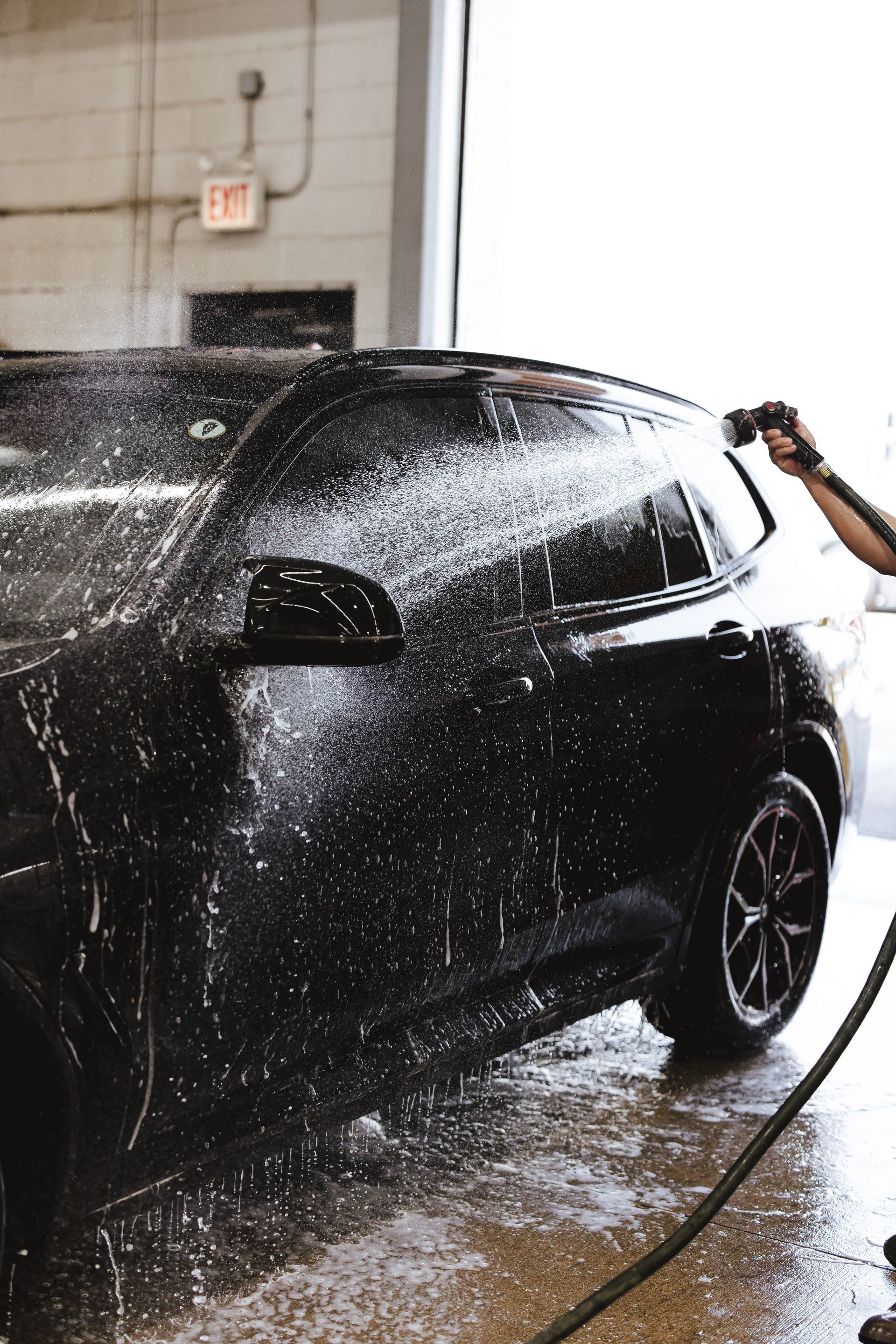 A man is washing a black car with a high pressure hose.
