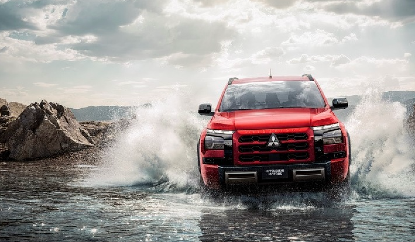 Uma caminhonete Mitsubishi vermelha atravessando um rio, criando grandes respingos.