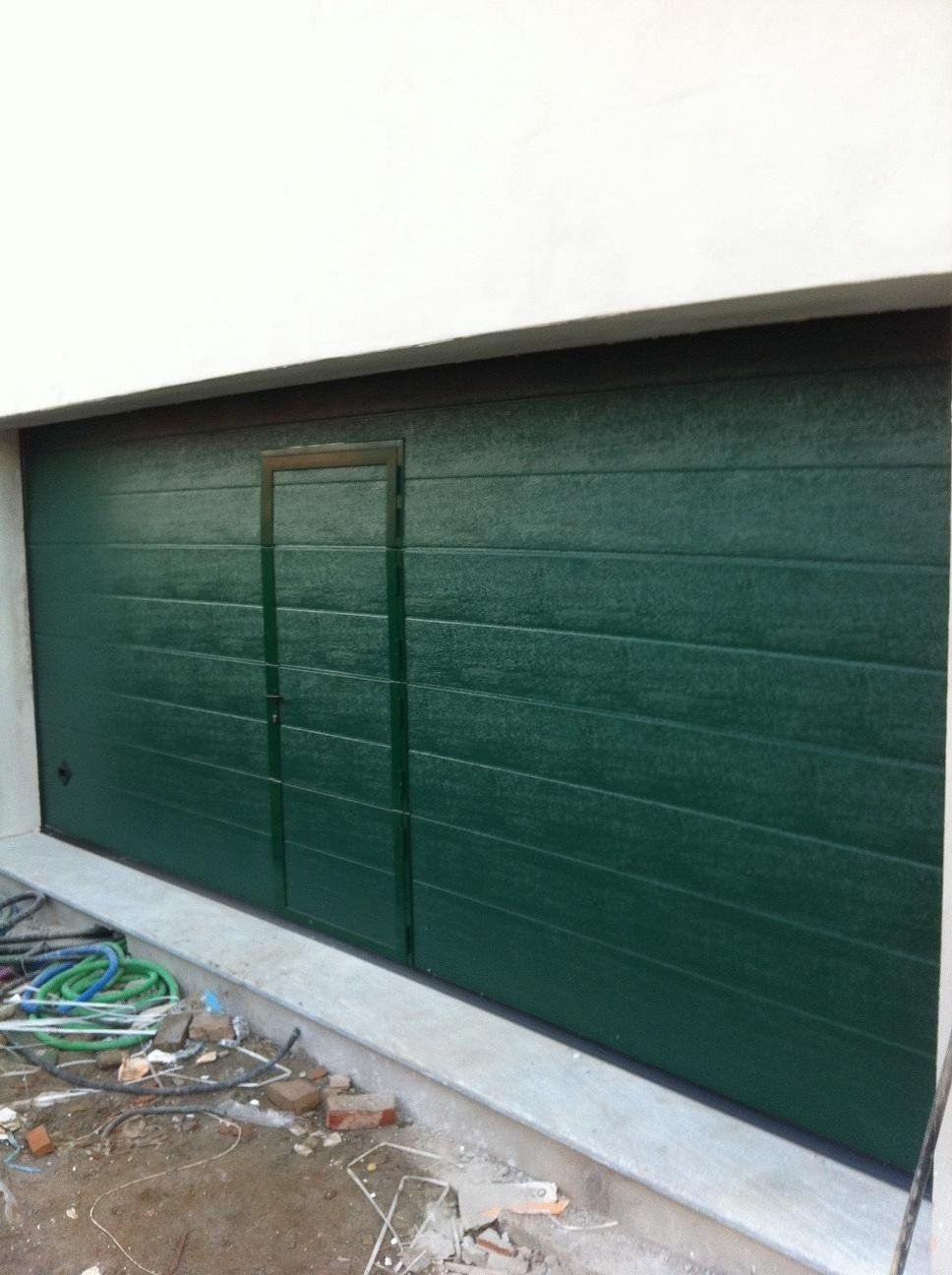 Una porta da garage verde è in fase di installazione sul lato di un edificio.