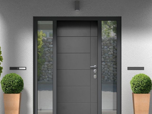 Porta d'ingresso grigia con luci laterali, piante in vaso e illuminazione moderna.