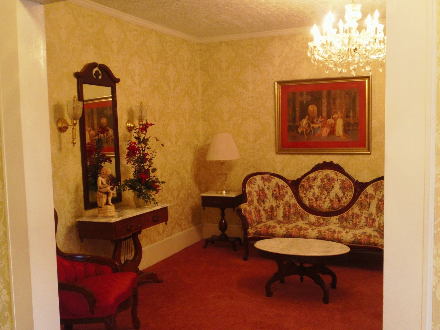 Elegant living room with floral sofa, red carpet, and ornate chandelier.