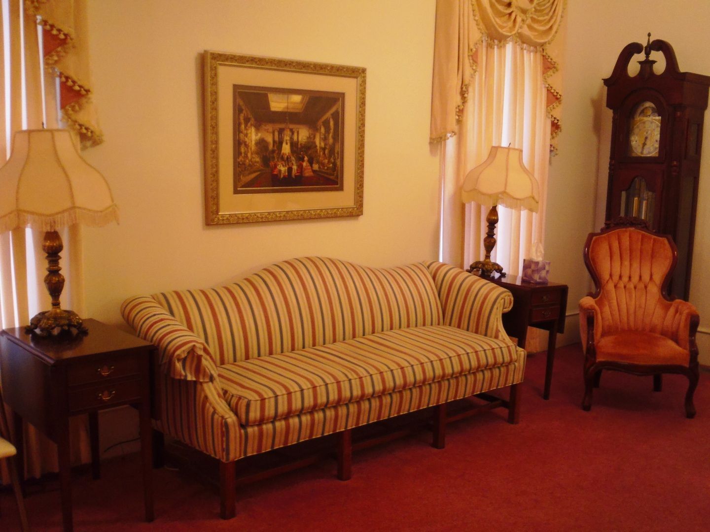 Formal living room with striped sofa, orange chair, and grandfather clock on red carpet.