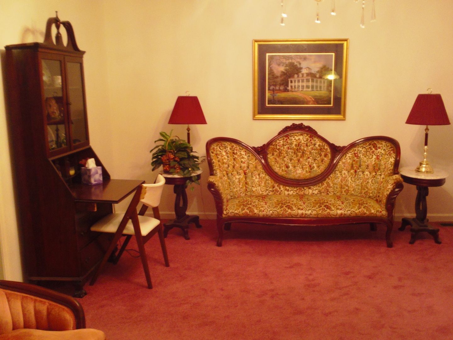 Living room with ornate sofa, matching lamps, mahogany desk, and red carpet.