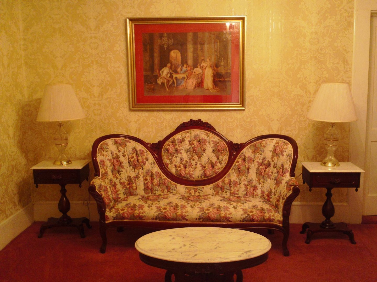 Living room with floral sofa, marble table, lamps, and artwork on a patterned yellow wall.