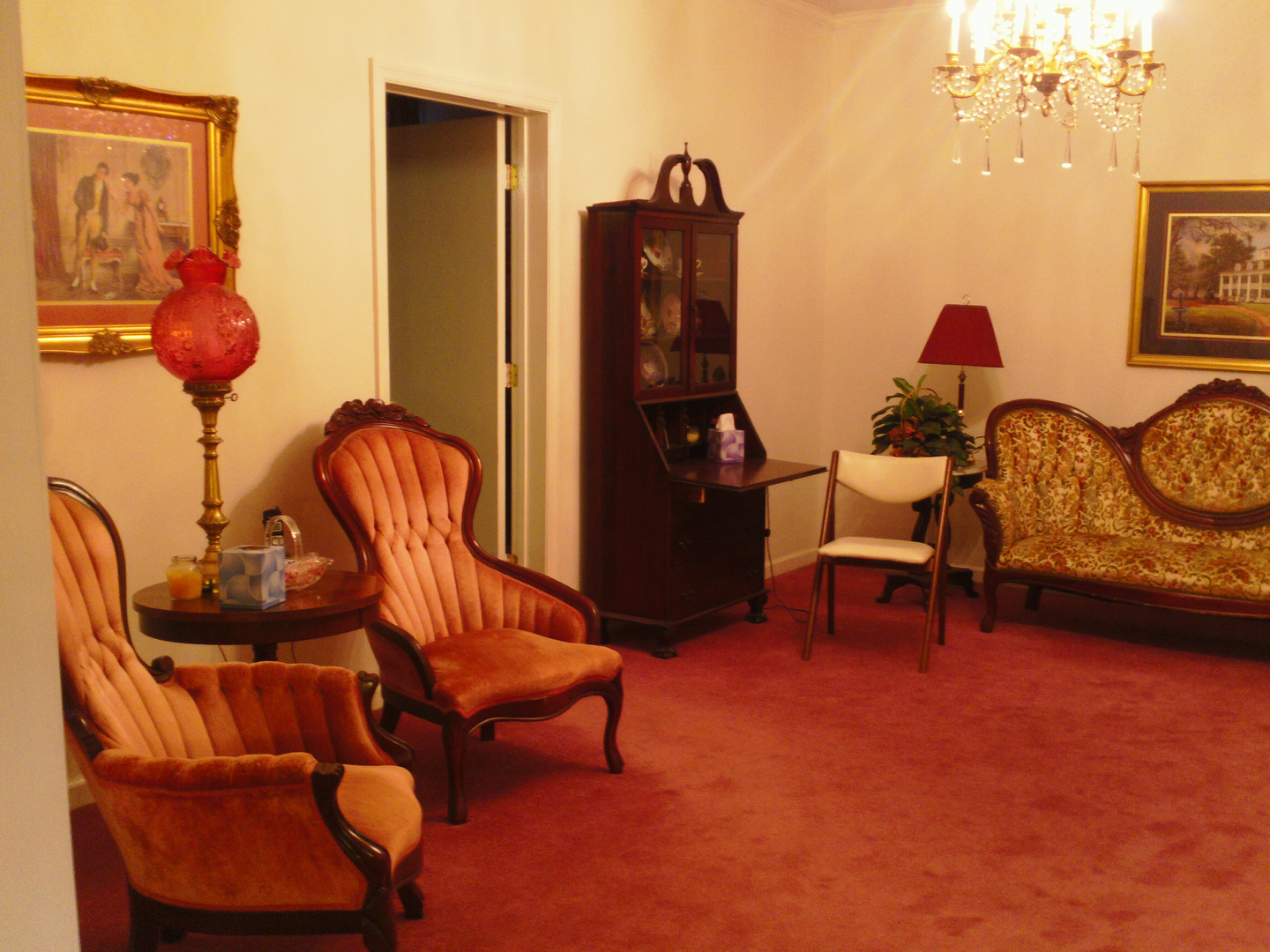 A room with antique furniture: orange chairs, a sofa, and a glass cabinet, on a red carpet.