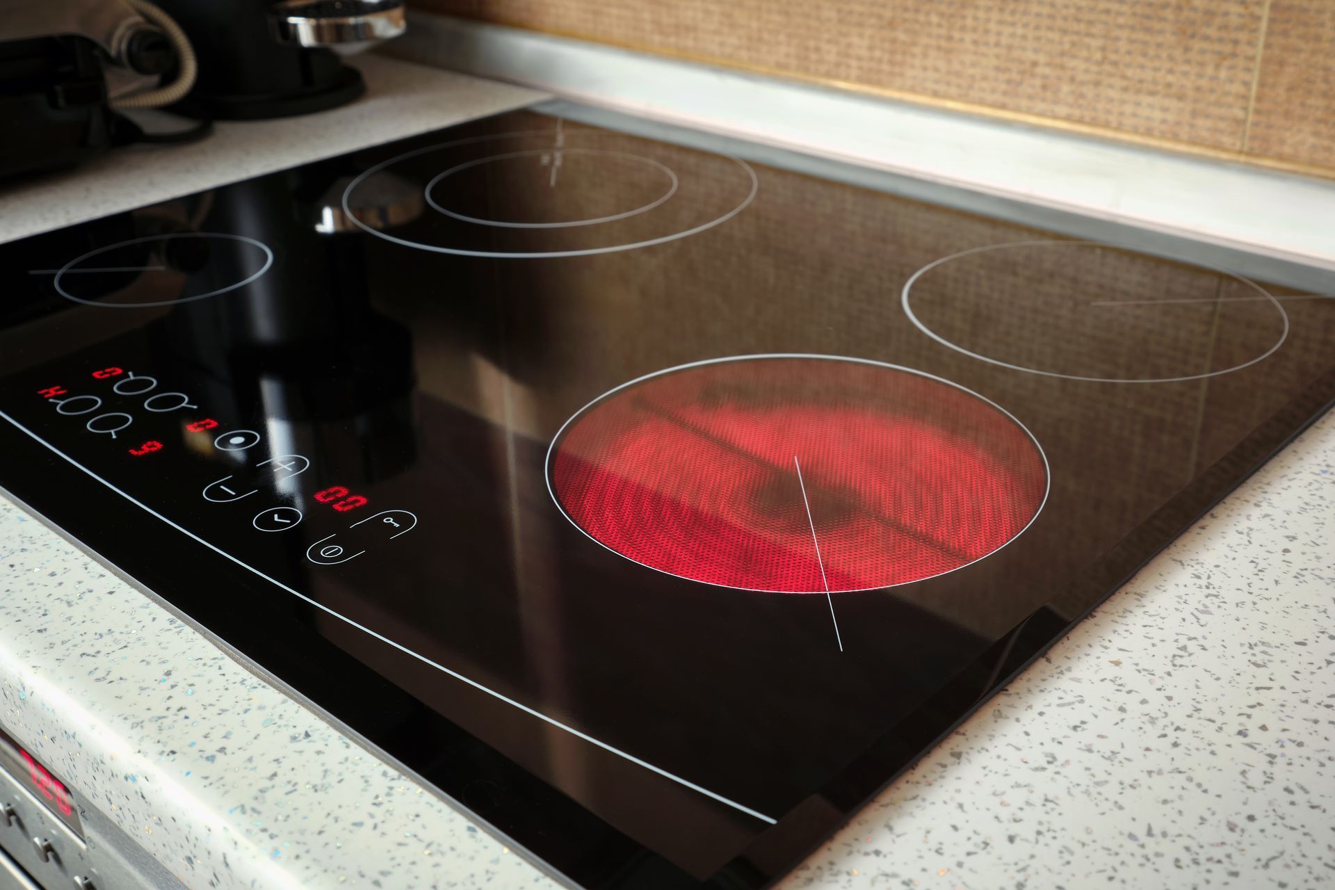 Black electric stovetop with one burner glowing red, other burners visible. Kitchen setting.