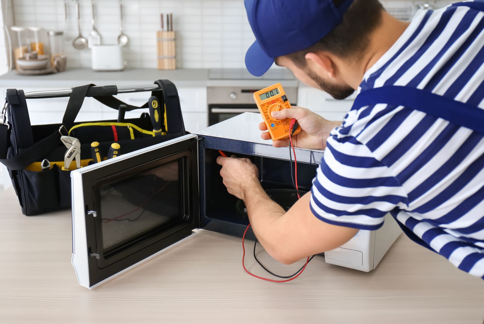A repairman checks a microwave with a multimeter in a kitchen.