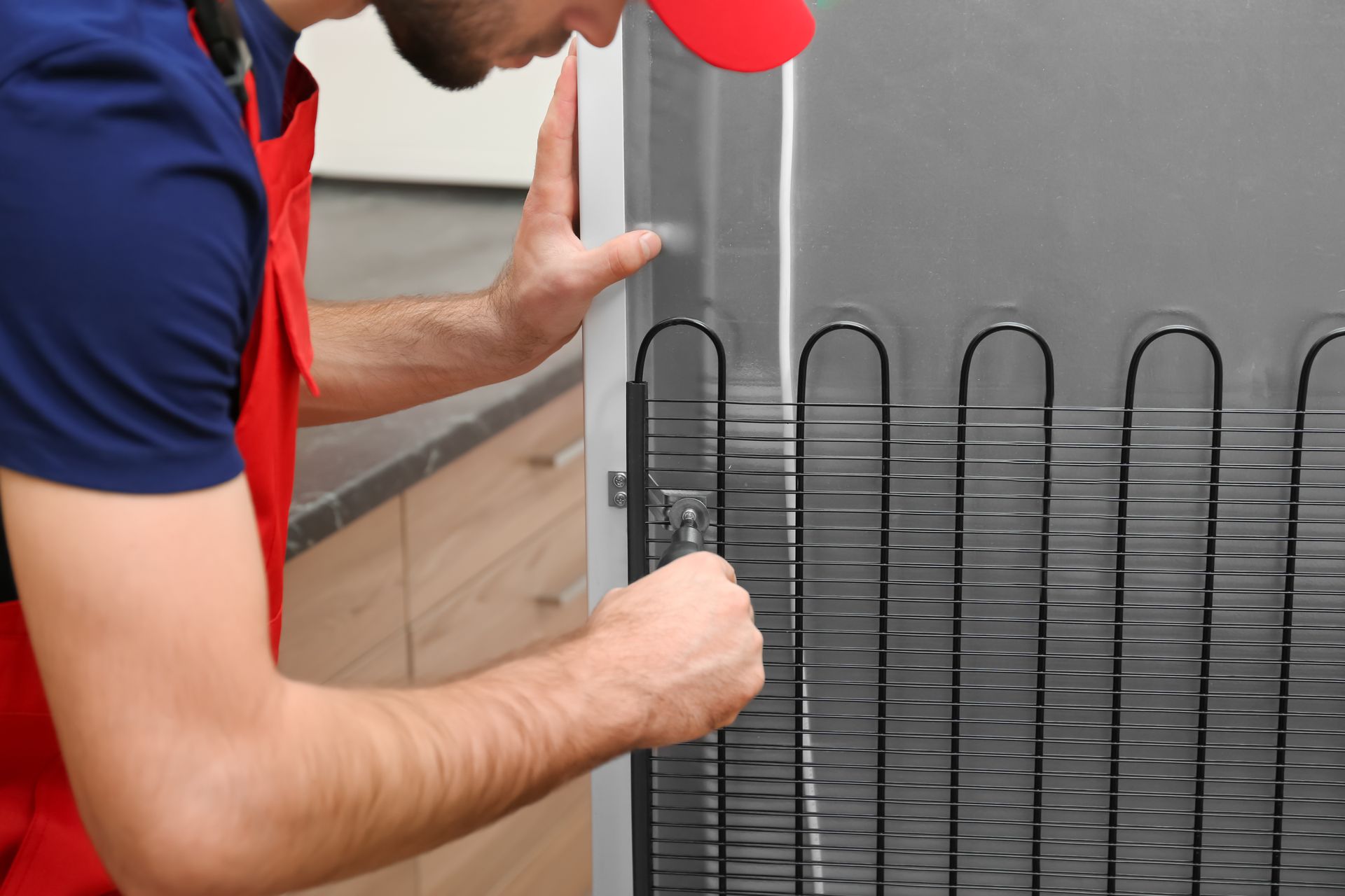 Person in red apron repairs refrigerator's cooling coils.