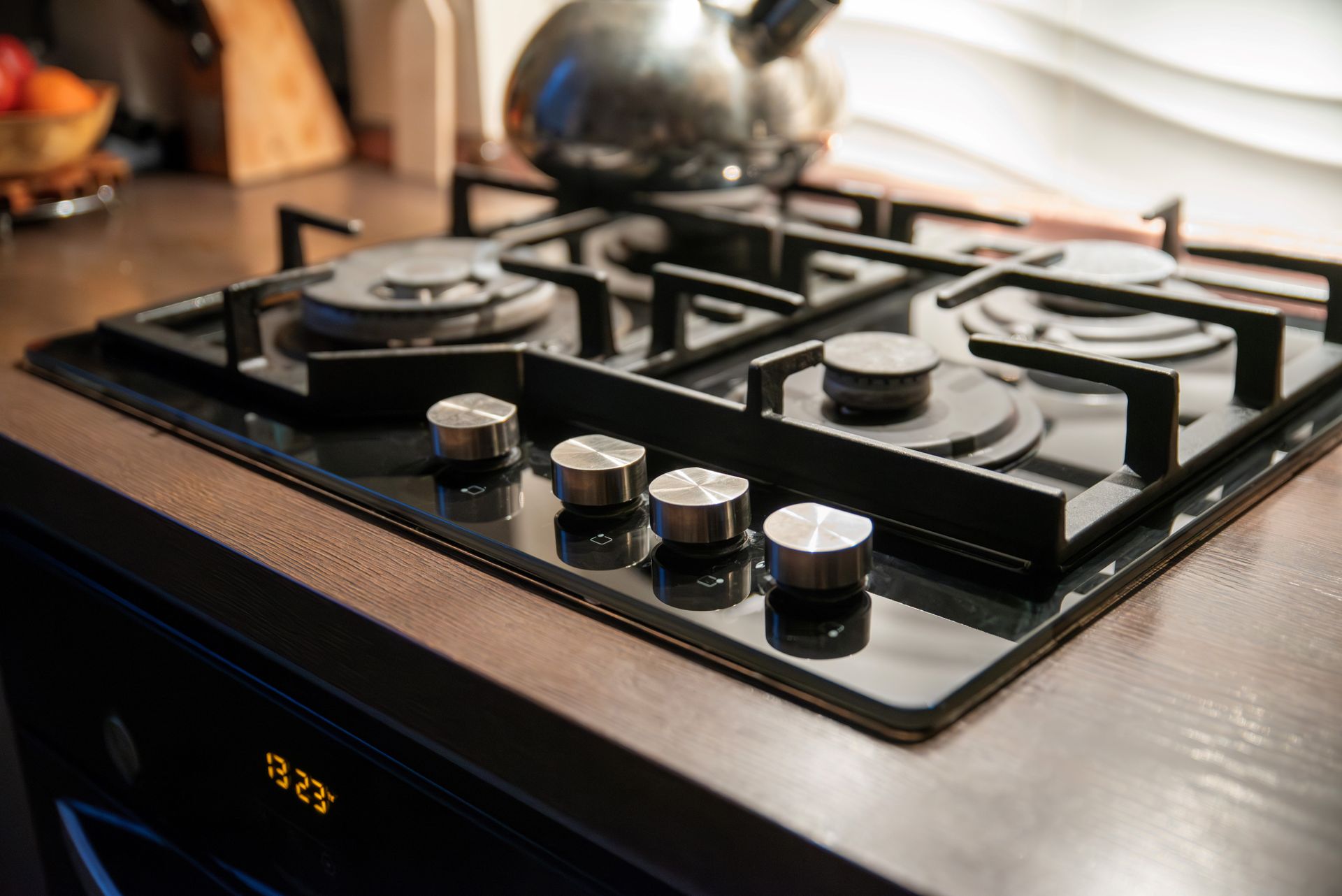 Gas stovetop with four burners, control knobs, and a kettle in a kitchen.