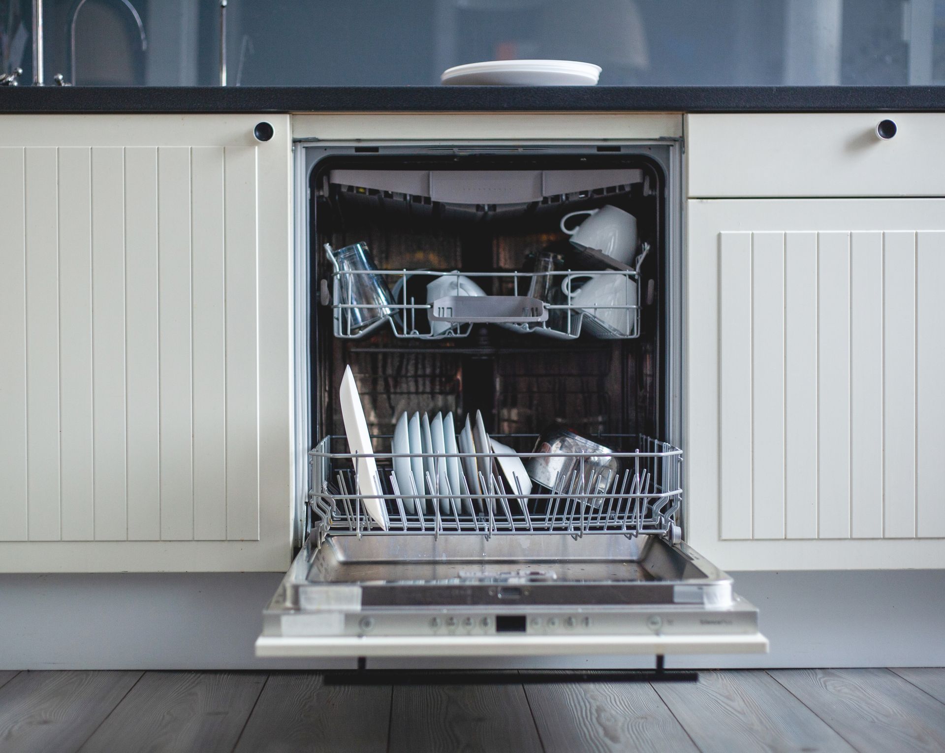 Dishwasher with door open, loaded with dishes and glassware in a kitchen.