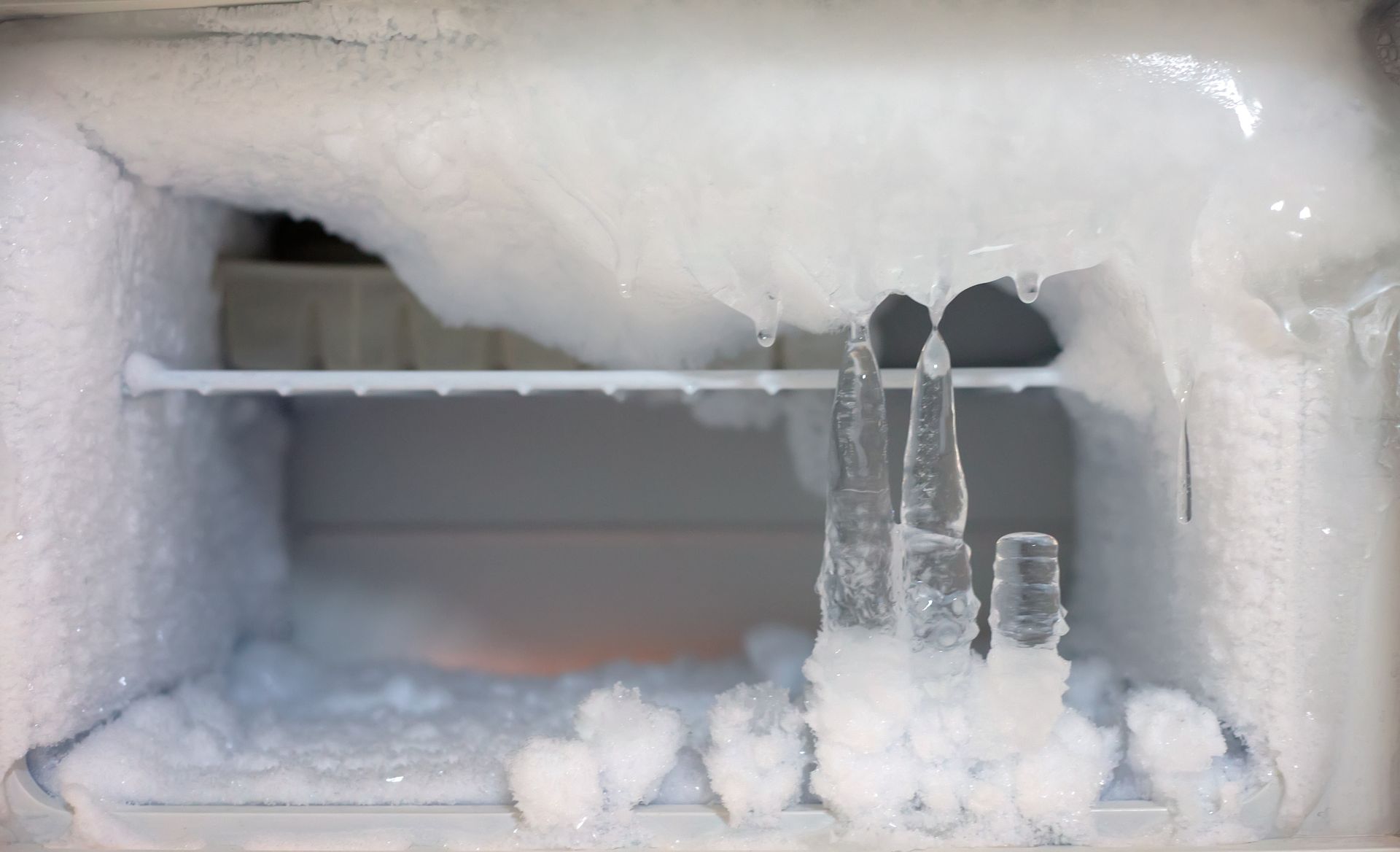 Interior of a freezer heavily coated in ice with large icicles hanging down.