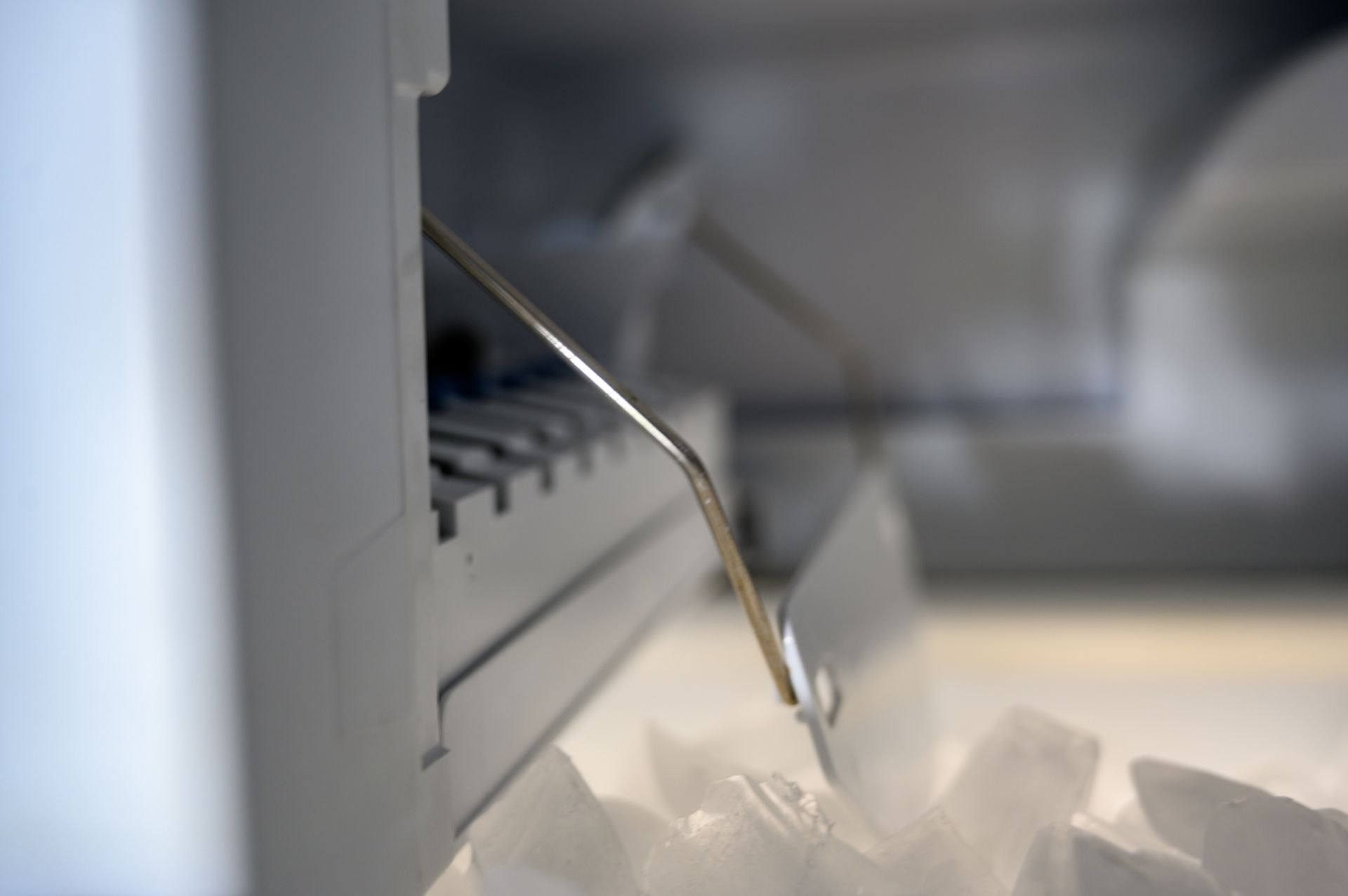 Inside a refrigerator: a metal arm pushing ice cubes from the ice maker into the bin.