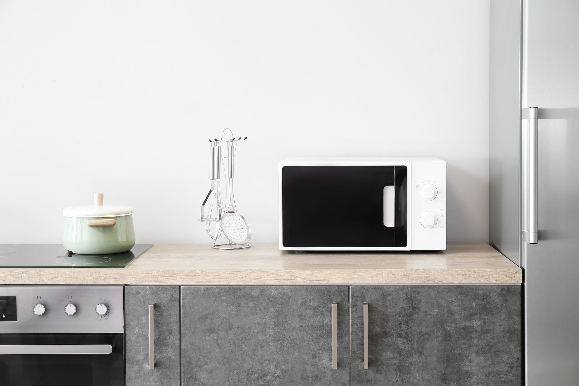 A white microwave on a kitchen counter with a pot and utensils next to it.