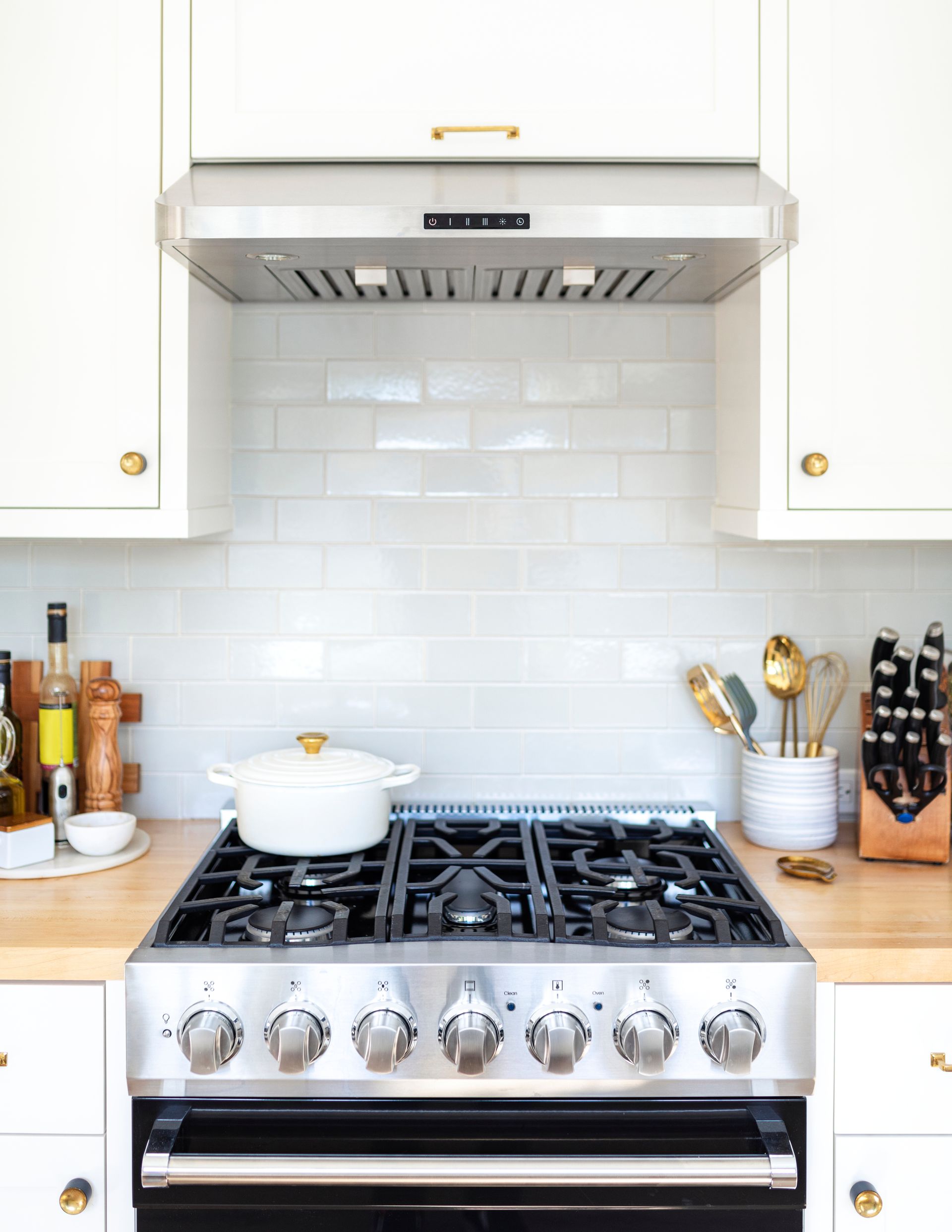 Stainless steel range in a white kitchen with a white pot.