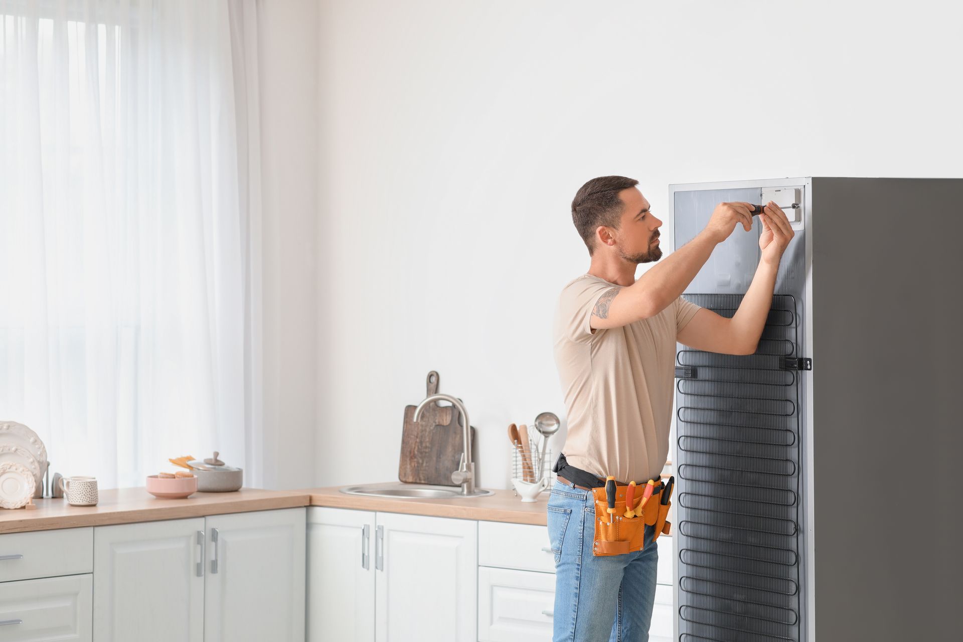 Man repairing refrigerator in a kitchen, using tools.