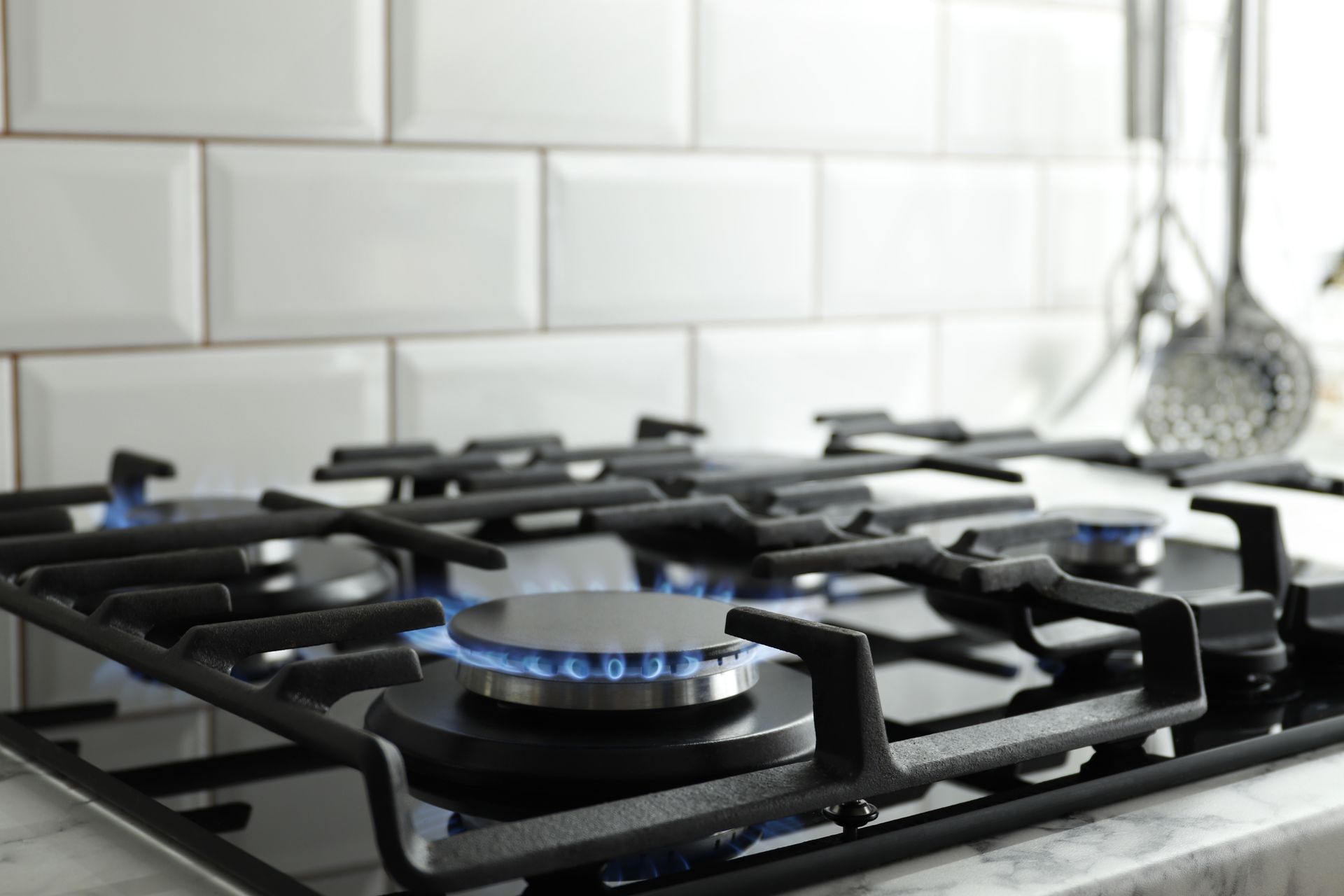 Gas stovetop with blue flame, black grates, white tile backsplash, kitchen setting.