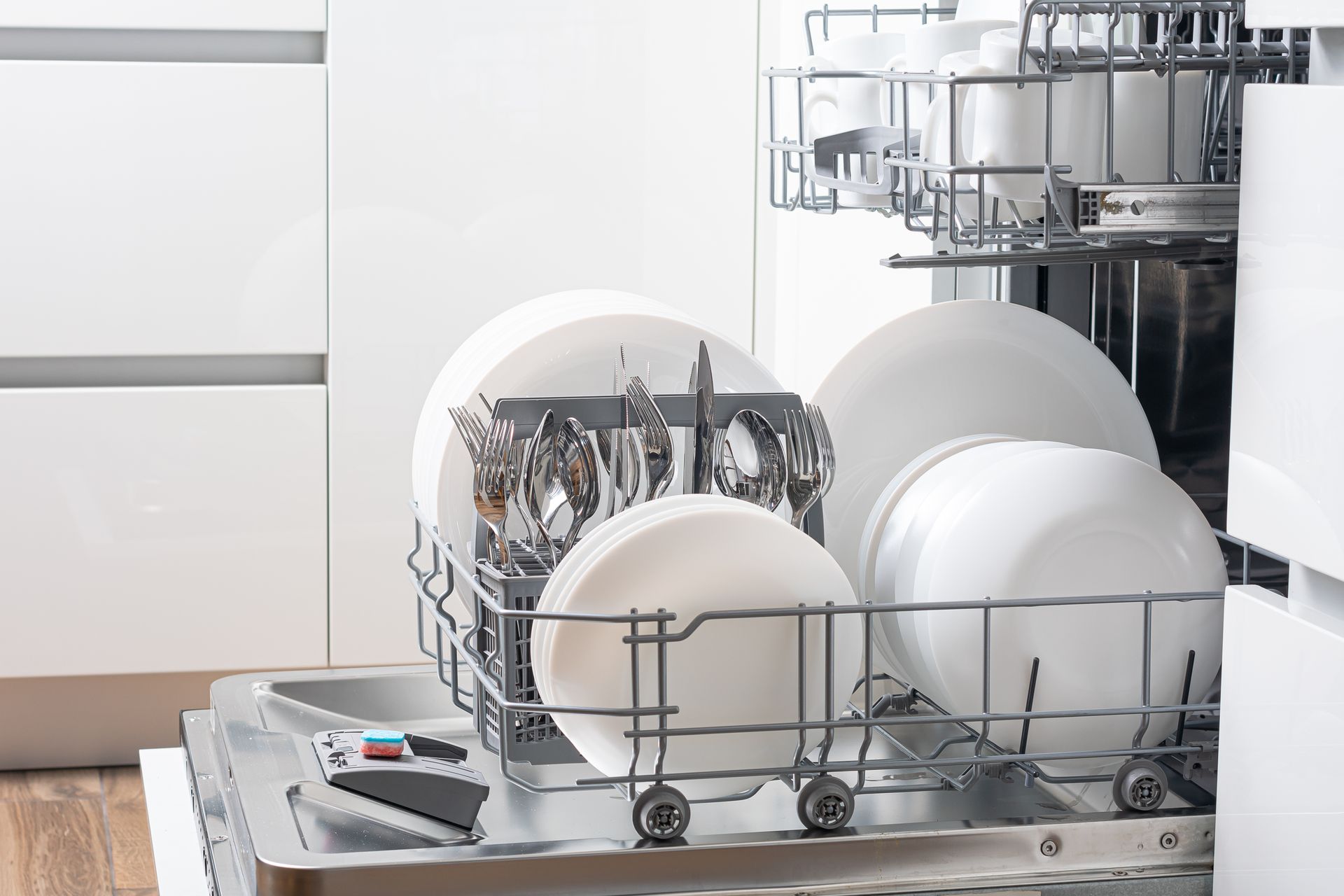 Dishwasher loaded with white plates, bowls, and silverware; stainless steel interior.