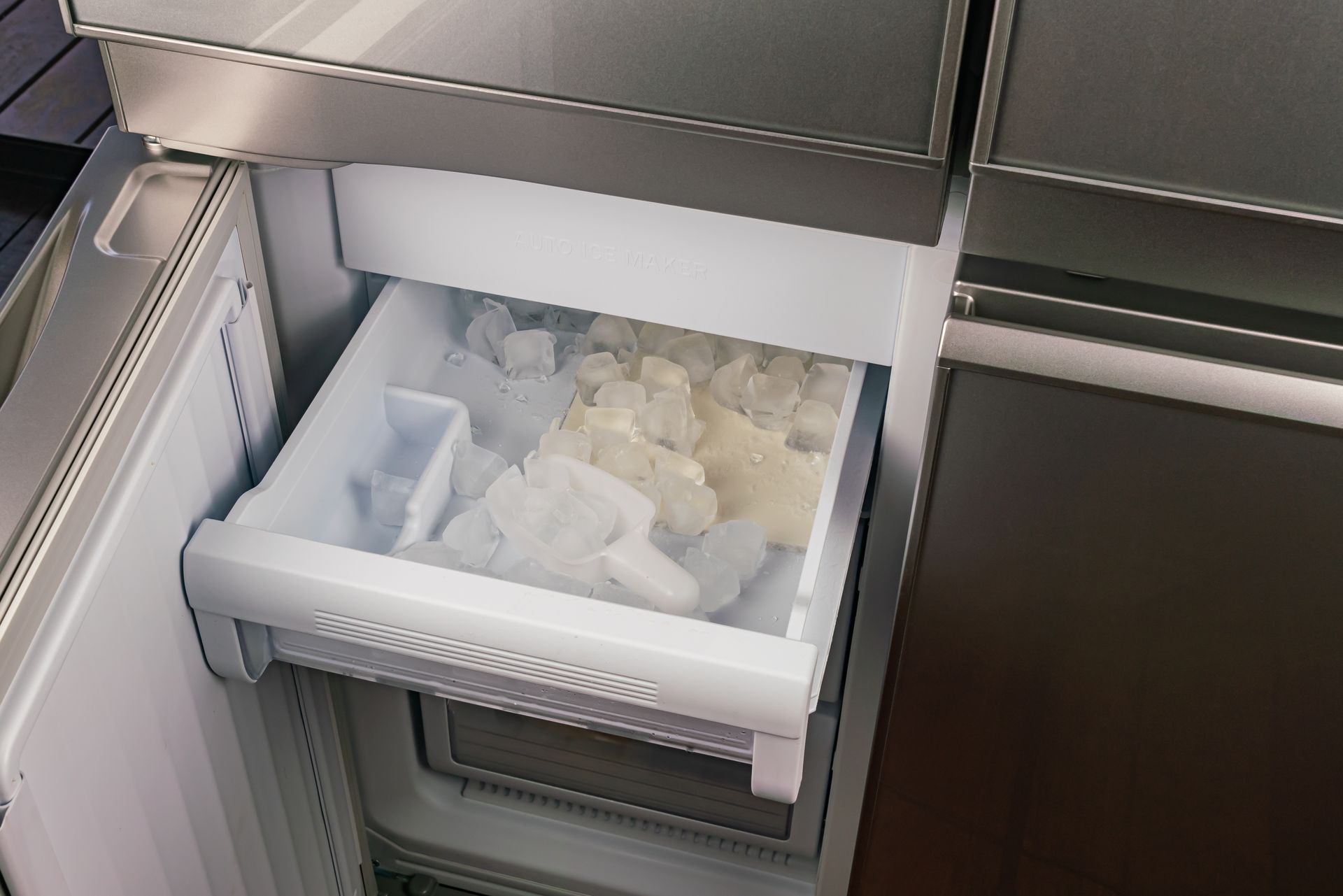 Refrigerator drawer open, filled with ice cubes in a compartment.
