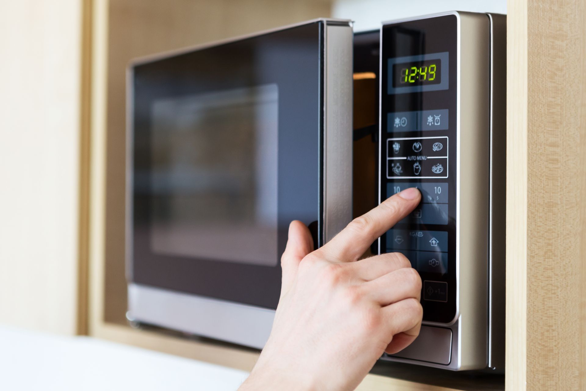 Hand pressing a button on a microwave, likely setting it to cook food.