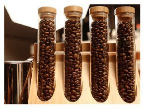 四根裝滿咖啡豆的玻璃管，放在一個木製支架上。每根玻璃管都有一個木塞。