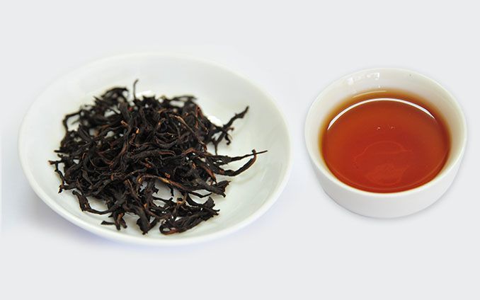 白色碟子裡盛著有機紅茶的茶葉,旁邊放著一杯深琥珀色的茶。