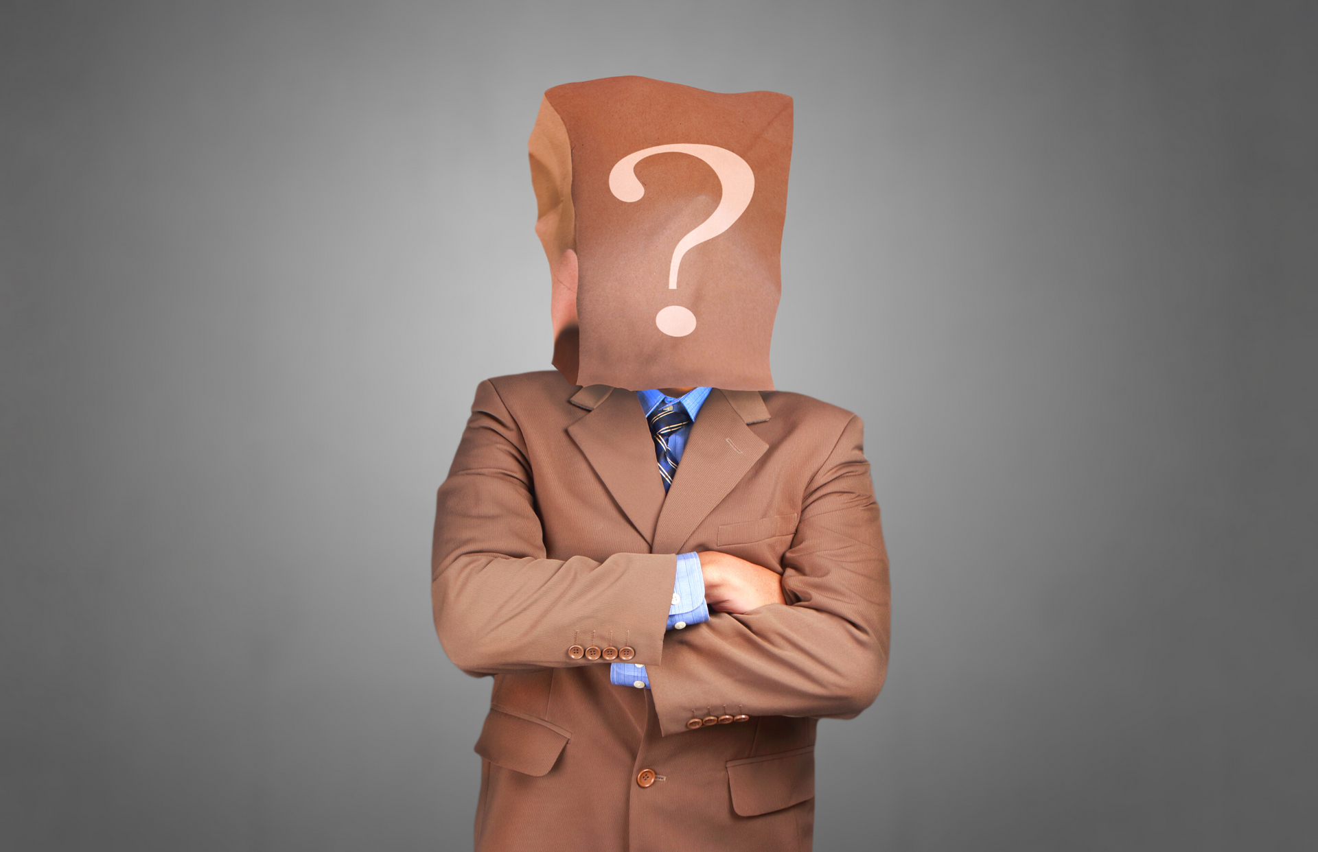 A man in a suit with a paper bag over his head with a question mark on it