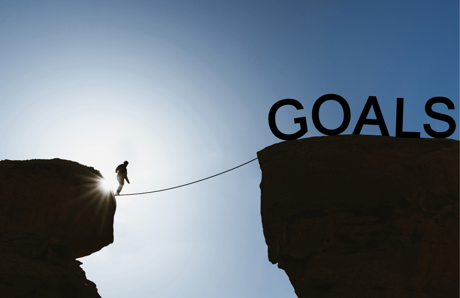 A man walking across a canyon to a cliff with the word goals written on it