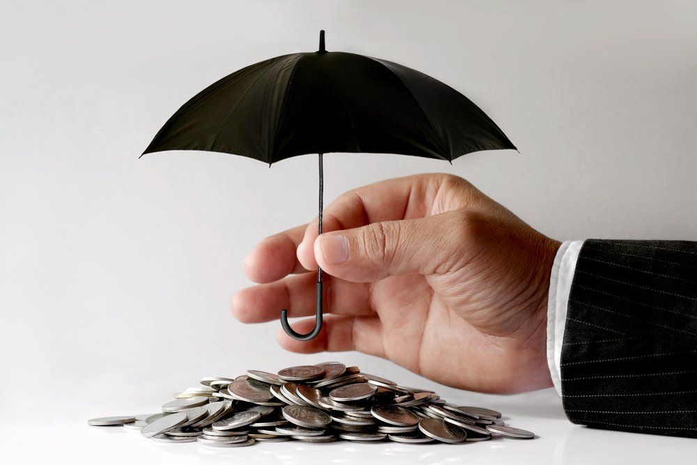 A hand holding an umbrella over a pile of coins.