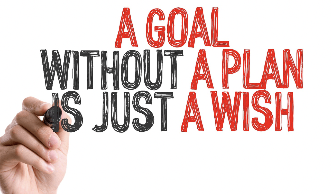 a hand writing out the phrase a goal without a plan is just a wish without a